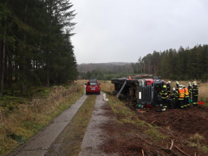 Náklaďák s dřevem skončil převrácený na boku mimo vozovku