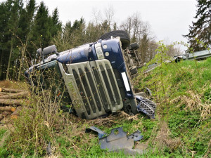 Kamion s nákladem dřeva nezvládl průjezd zatáčkou, položil se na bok a zřítil ze svahu