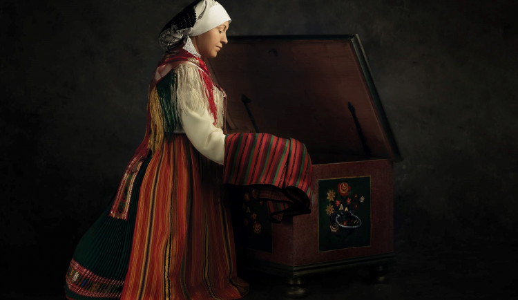 Mondolka. Právě tak se říkalo sukni, kterou vidíte na fotce. Na Chodsku měla každá bohatší nevěsta dvě takové malované truhly plné krojů. Koláč. Tak se zase označoval čepec, který má žena na hlavě. Kotě. Neboli proutek je omotaný koudelí a plátnem, který