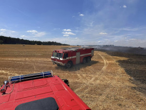 V příšerném vedru bojují hasiči s obrovským požárem pole a lesa na ploše 25 hektarů. Hořet začalo od balíkovače
