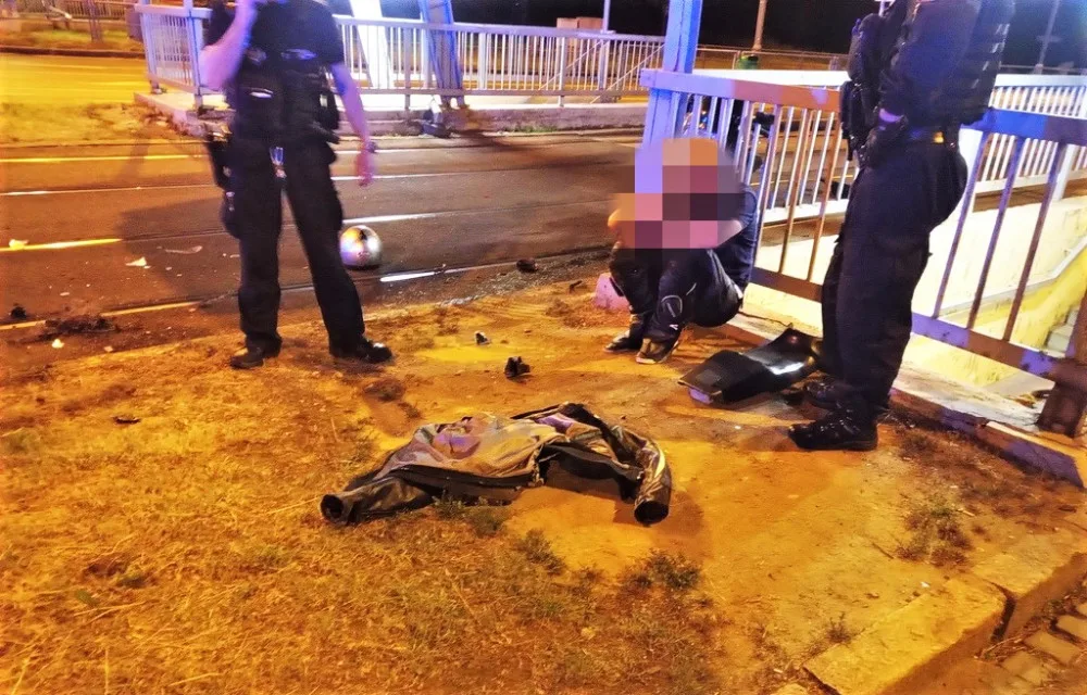 Strážníci hlídají motorkáře, který havaroval se svým strojem. Kolem leží trosky jeho motorky