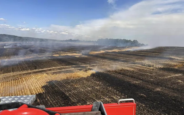 V příšerném vedru bojují hasiči s obrovským požárem pole a lesa na ploše 25 hektarů. Hořet začalo od balíkovače